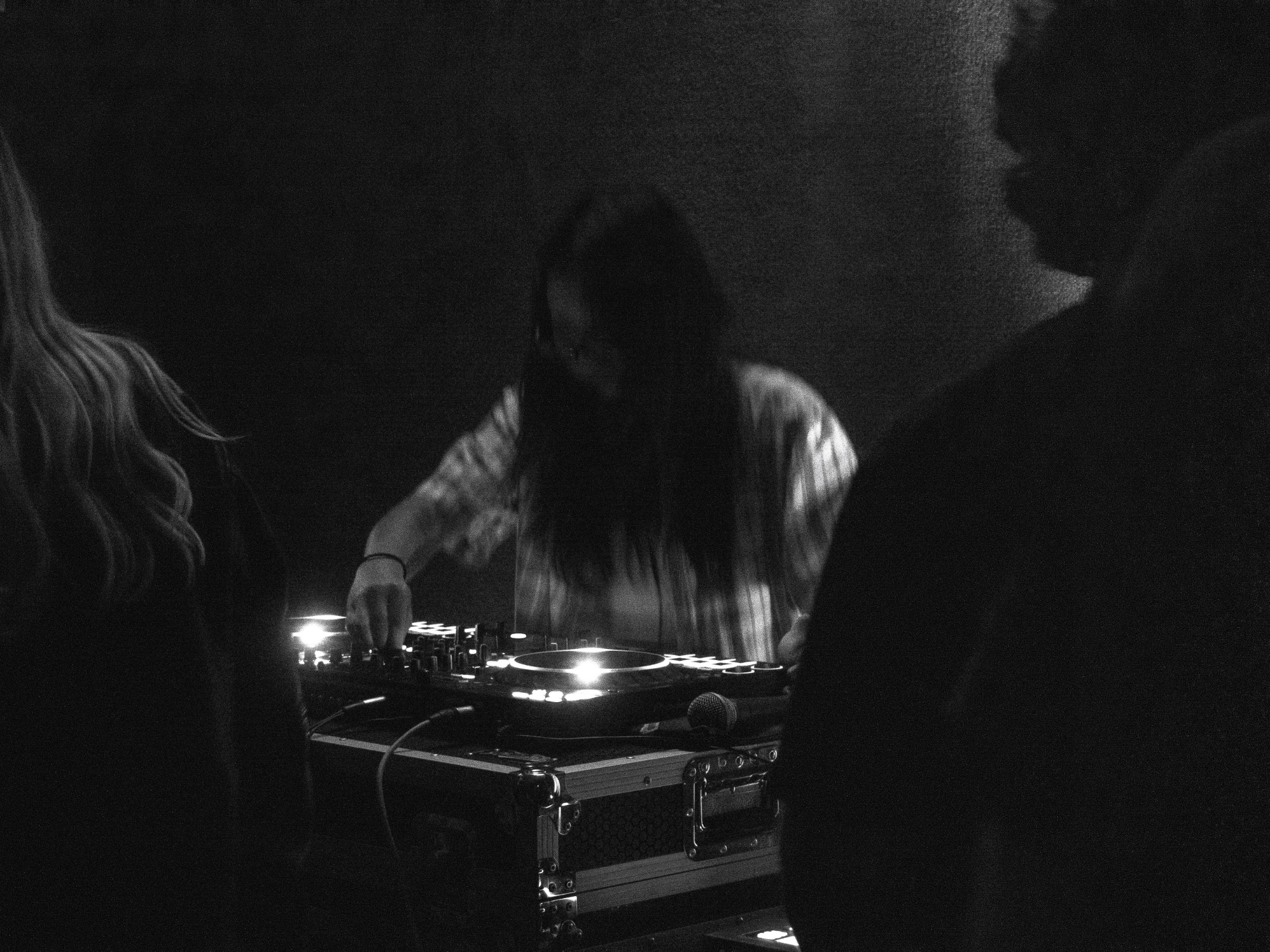 Black-and-white photograph of a DJ adjusting the mixing console