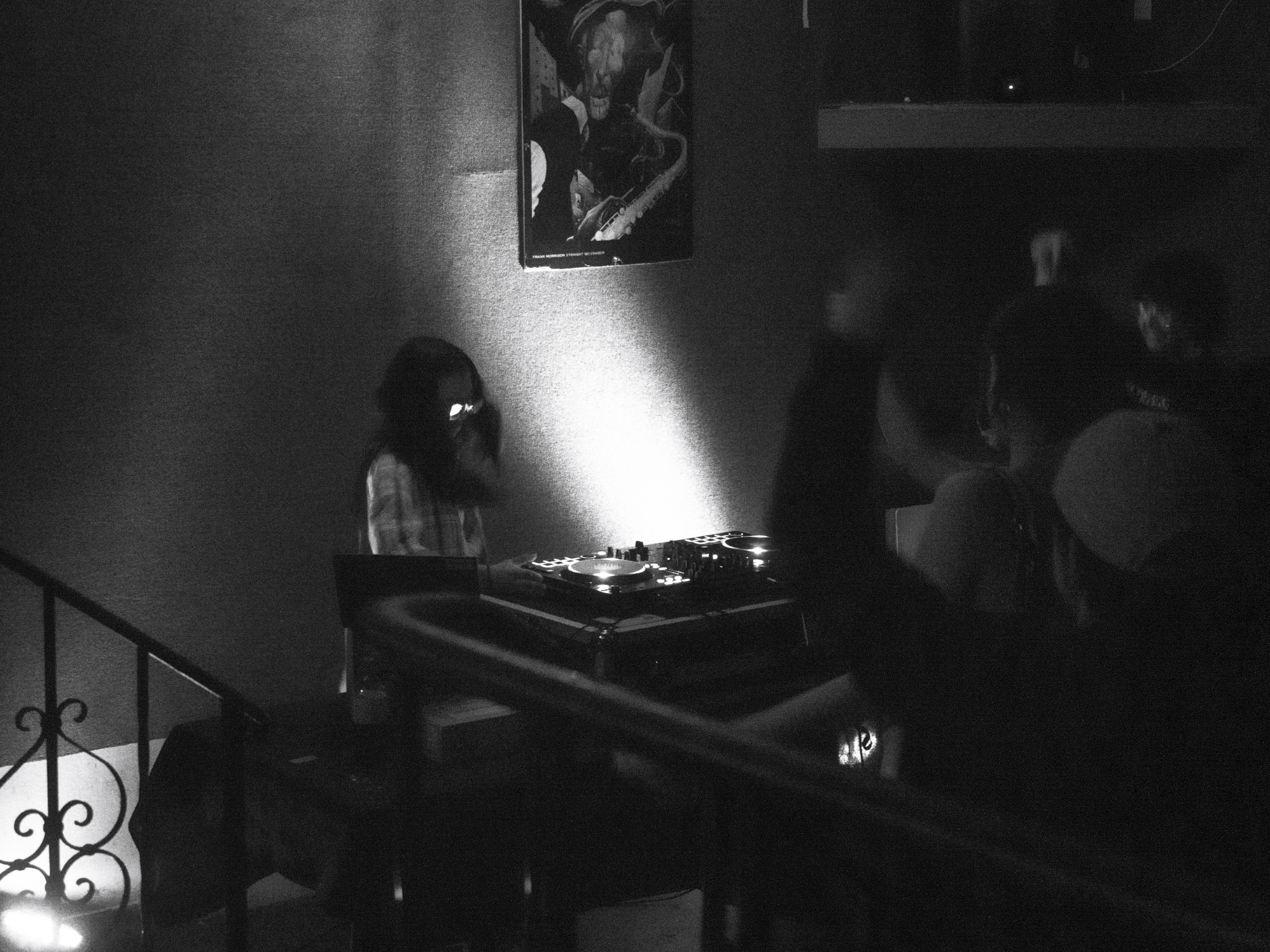 Black-and-white photograph of a DJ performing beside a stairway